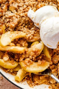 close up shot of cooked apples in an apple crisp with ice cream scoops to the side