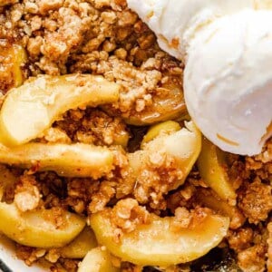 close up shot of cooked apples in an apple crisp with ice cream scoops to the side