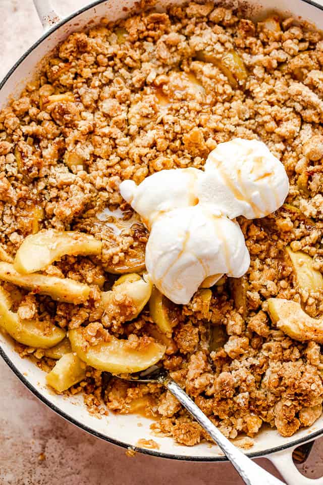 top shot of apple crisp in a round baking dish topped with three scoops of vanilla ice cream