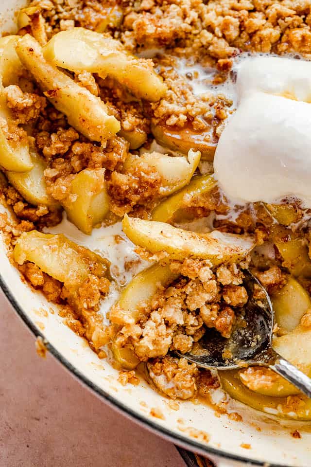 large silver spoon scooping out apple crisp from baking dish