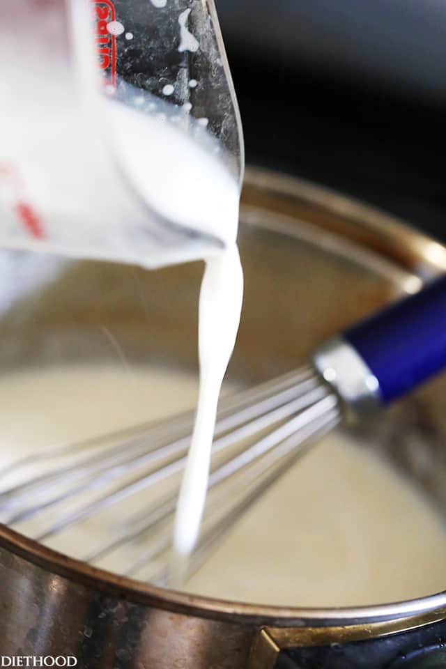 Milk being added to a roux of flour and butter in a saucepan, with a whisk.