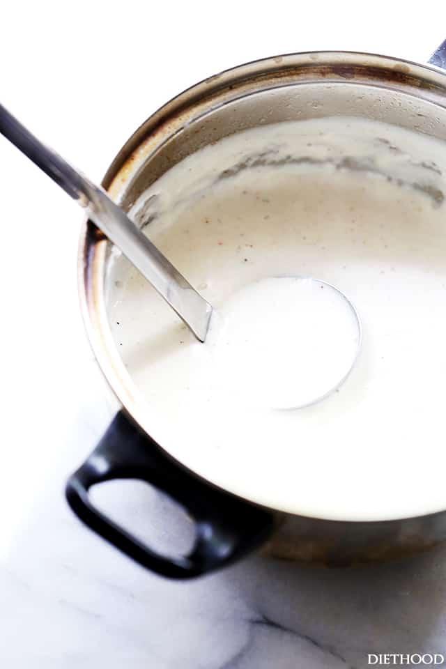 A ladle resting in a pot of bechamel sauce.