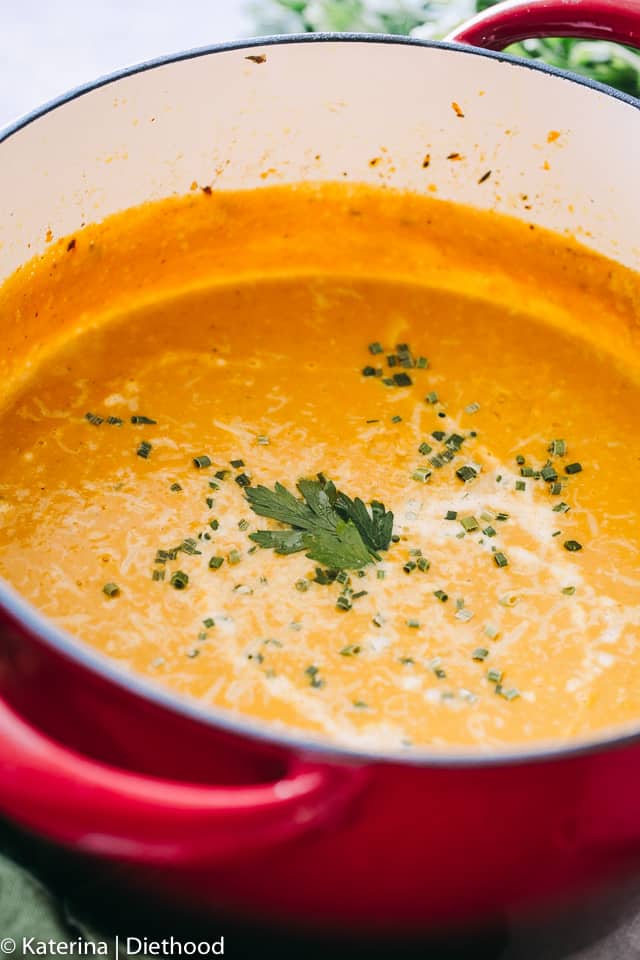 Butternut squash soup garnished with fresh herbs in a large red pot.