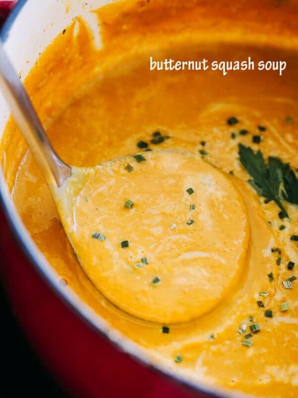 A ladle lifting creamy butternut squash soup from a large red pot.