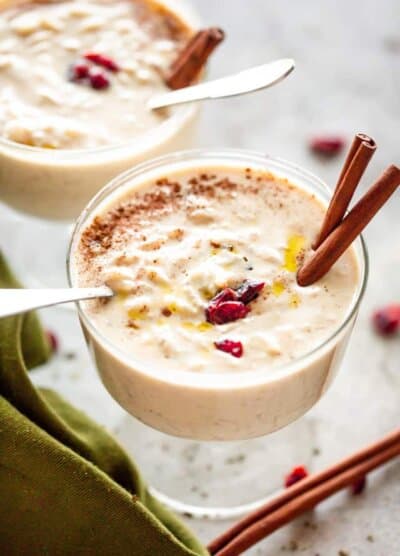 Creamy Rice Pudding Dessert in a glass cup, garnished with two cinnamon sticks and dried cranberries.