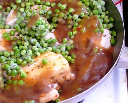 Chicken Breast with sauce and frozen peas in a skillet