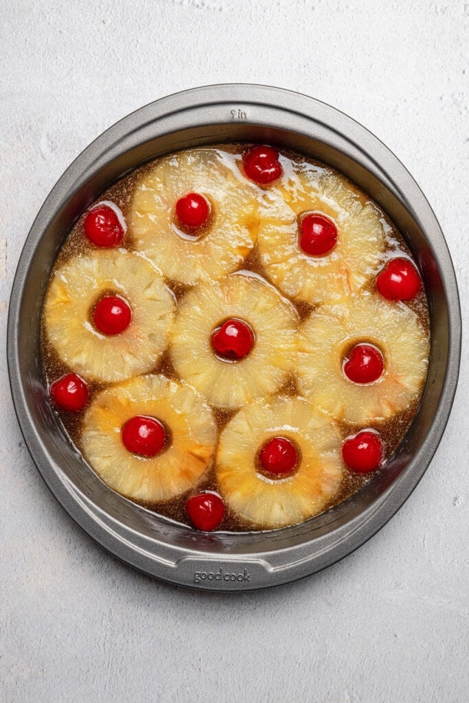 Pineapple rings and maraschino cherries arranged over the brown sugar topping in the bottom of a baking pan.
