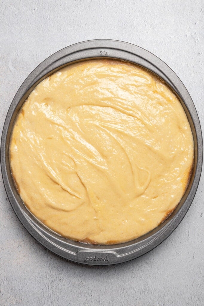 Pineapple upside down cake batter spread over top of the pineapple layer in a round cake pan.