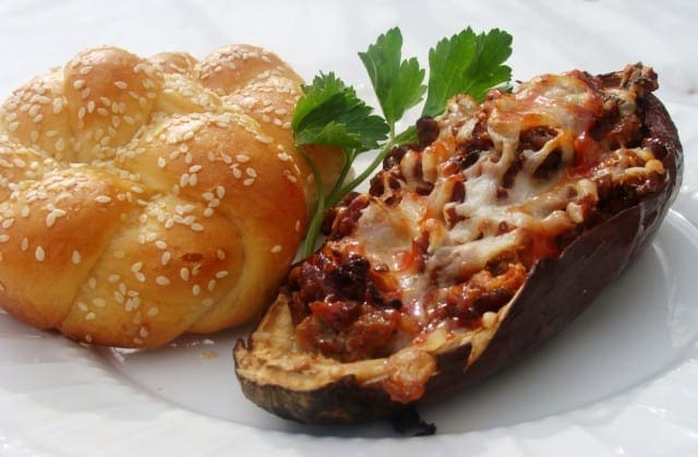 Close-up view of Sausage Stuffed Eggplant next to a sesame roll on a plate