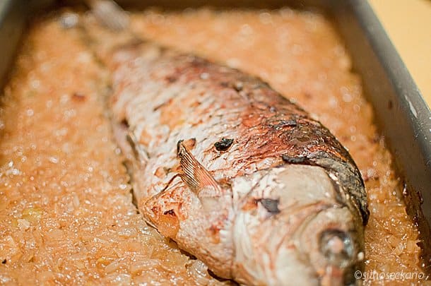 Whole baked carp fish on a layer of caramelized onions