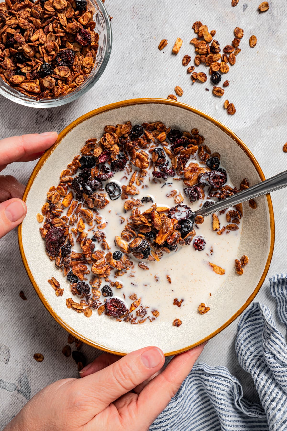 Overhead photo of a bowl with chocolate granola and milk. Two hands are holding the bowl.