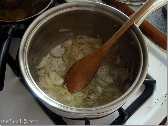 Overhead view of onions and garlic cooking in a saucepan with a wooden spoon