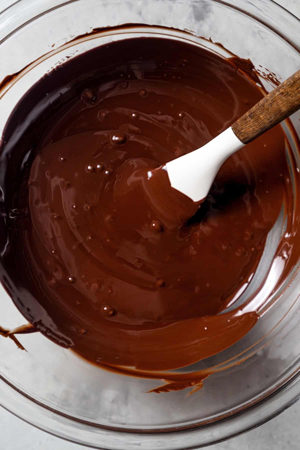 Melted chocolate in a glass bowl with a spatula.