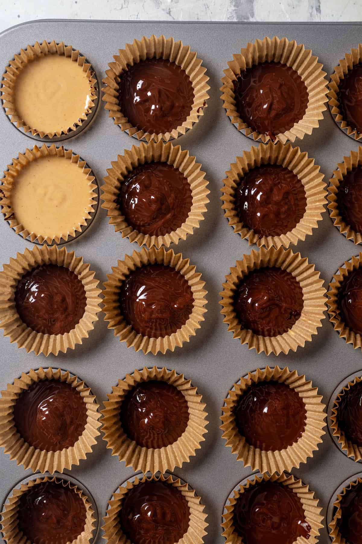 Partially assembled peanut butter cups inside a lined 24-cup muffin pan.