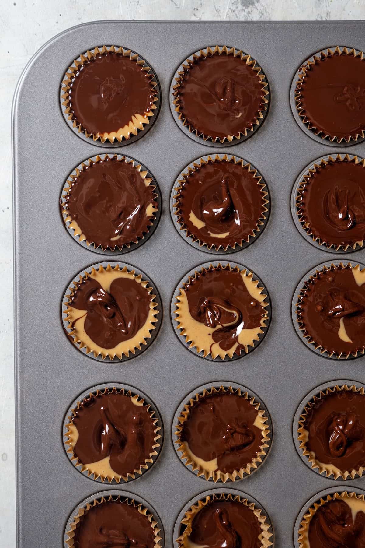 The top chocolate layer added to peanut butter cups inside a lined 24-cup muffin pan.