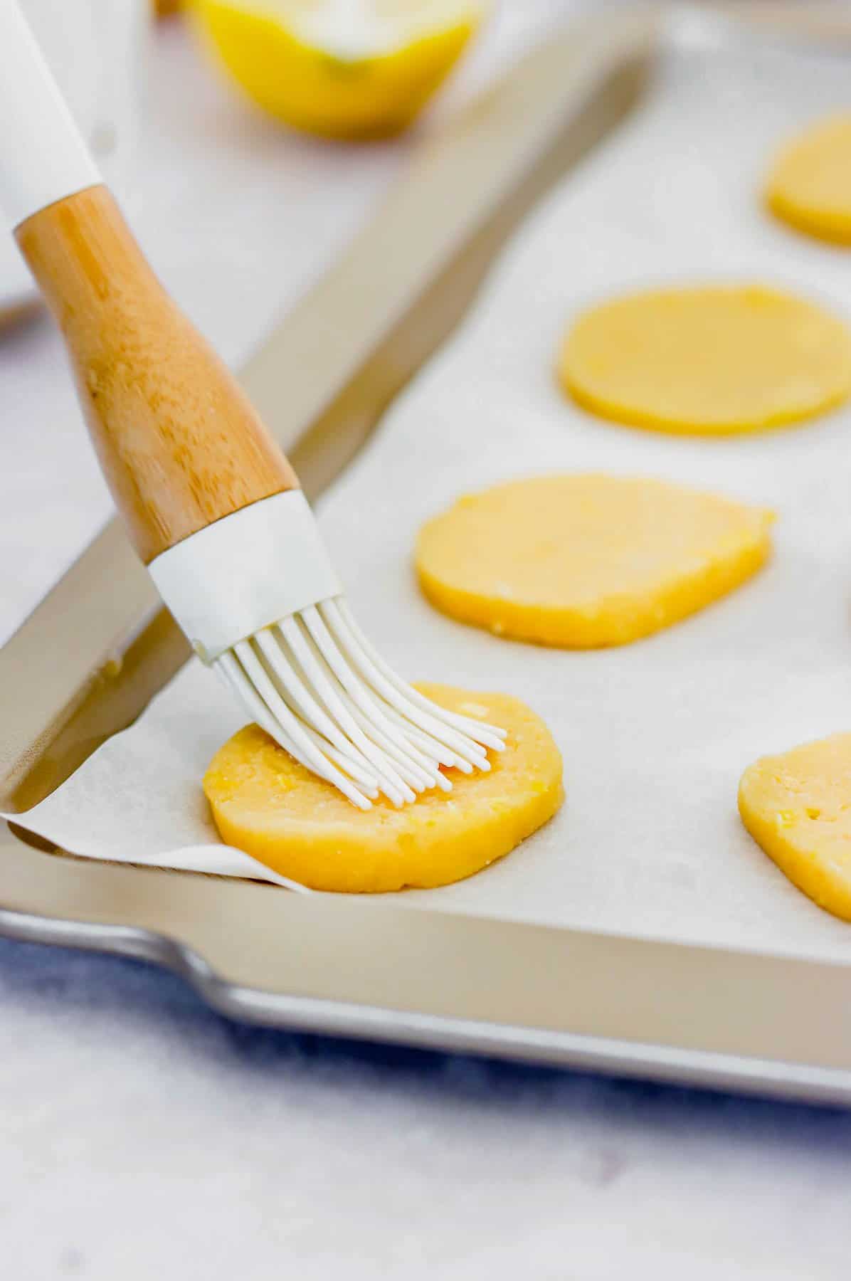 Cookies on a baking tray being coated with egg