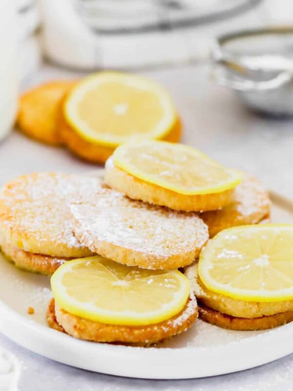 A plate of lemon cookies topped with lemon slices and dusted with powdered sugar.