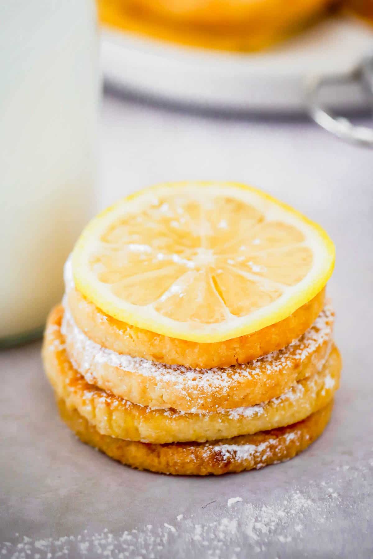 Lemon cookies stacked on top of each other in front of milk