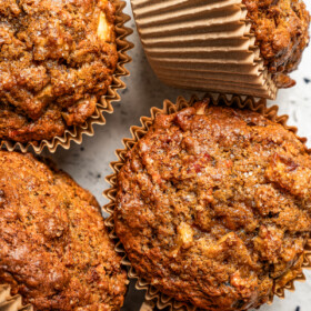 Photo of five morning glory muffins set on a light-colored surface.