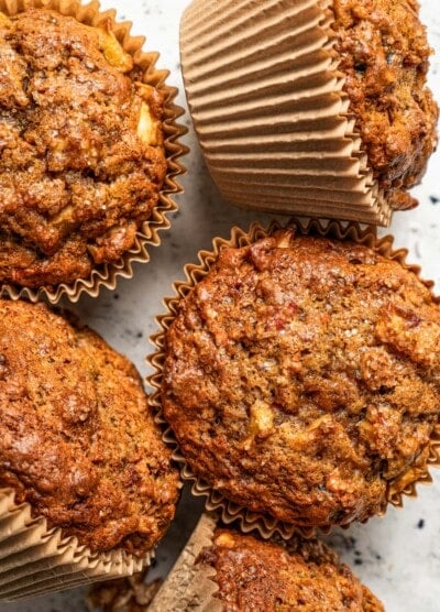 Photo of five morning glory muffins set on a light-colored surface.