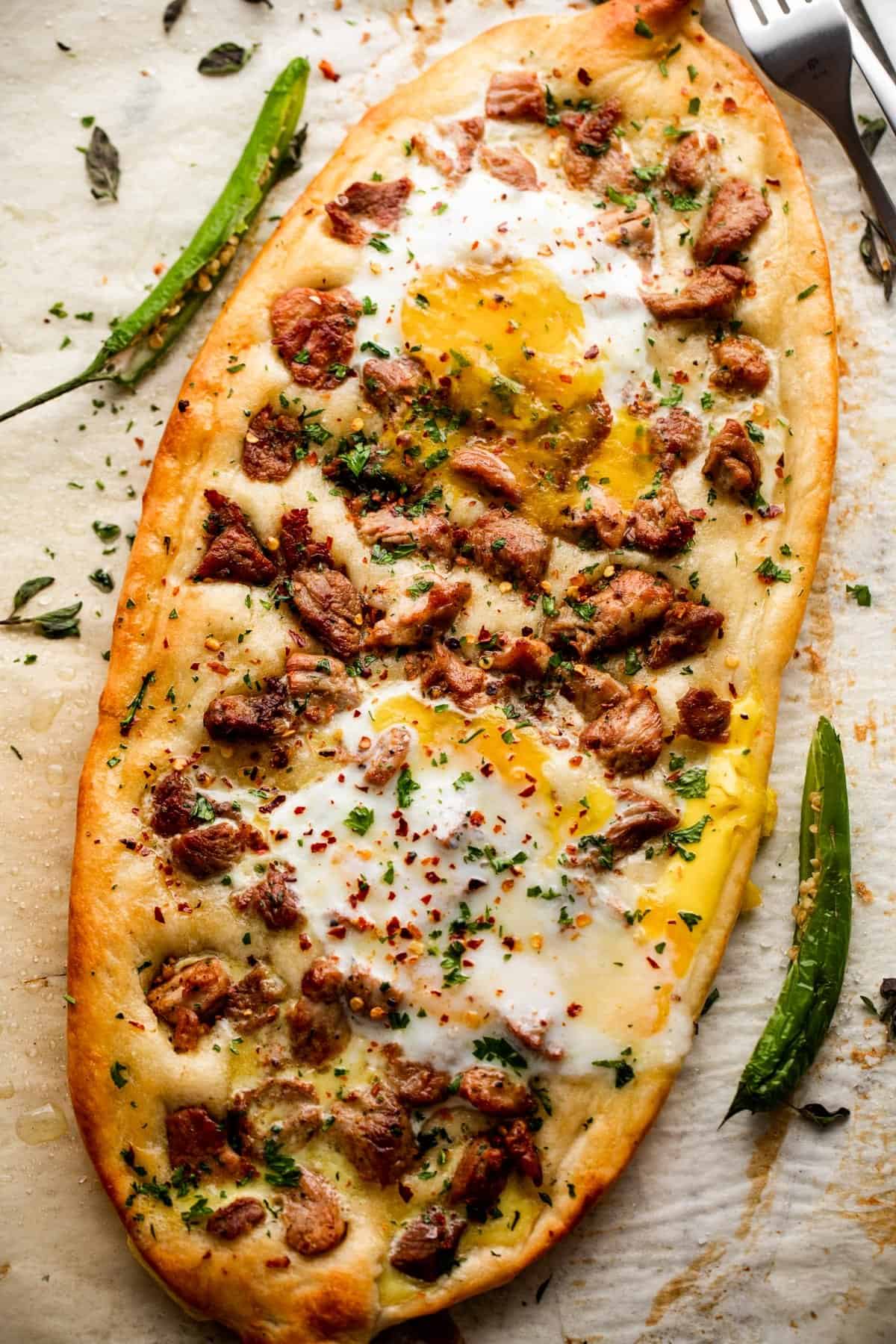 overhead shot of an oval shaped pizza topped with chunks of pork and fried eggs.