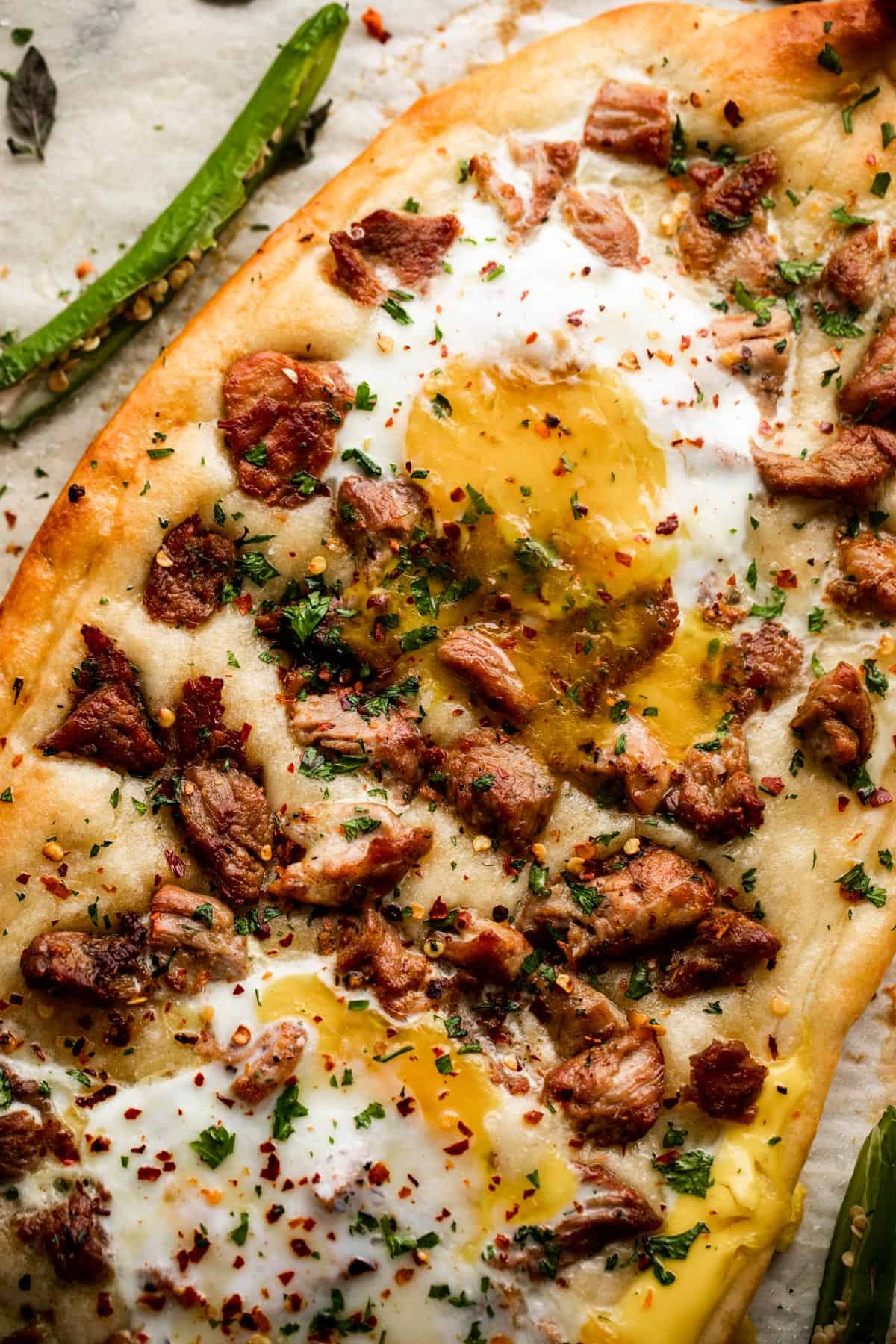 close up shot of Pastramajlija pizza topped with chunks of pork and fried eggs.