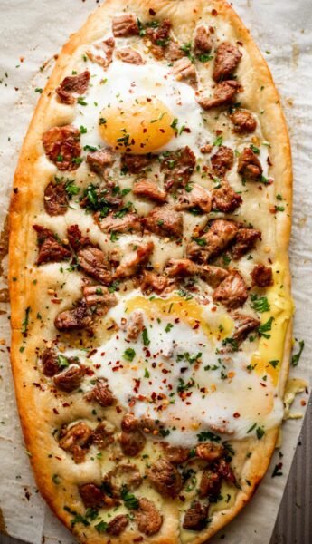 overhead shot of Pastrmajlija pizza topped with chunks of pork and fried eggs.