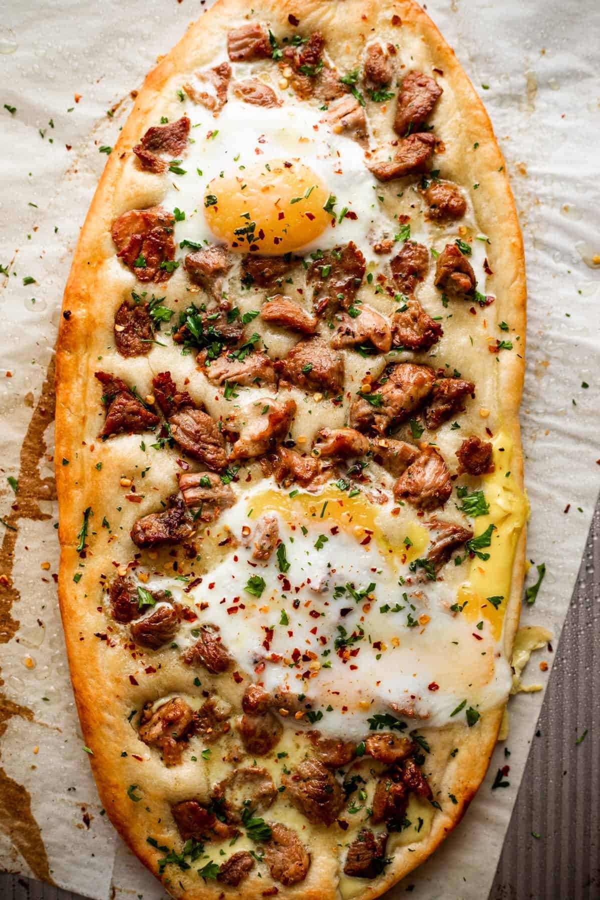 overhead shot of Pastrmajlija pizza topped with chunks of pork and fried eggs.