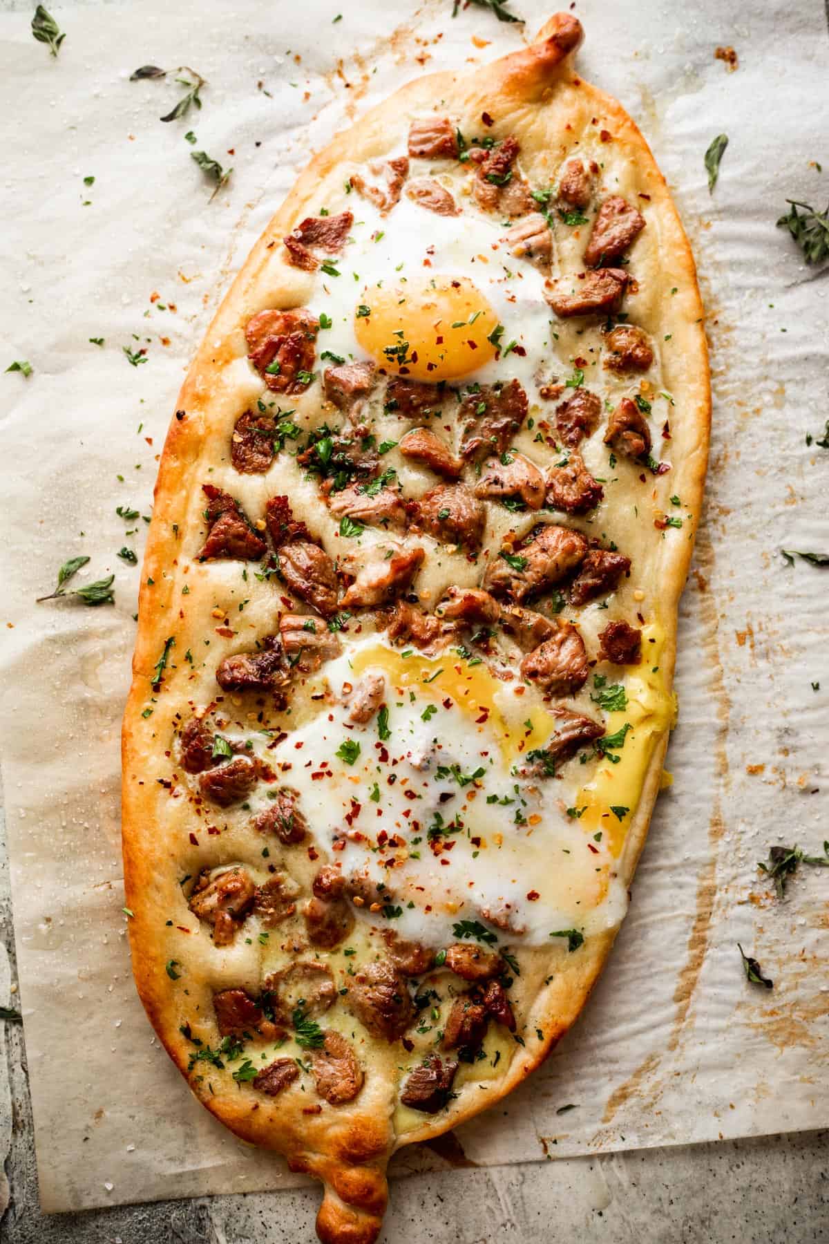 overhead shot of an oval shaped pizza topped with chunks of pork and fried eggs.