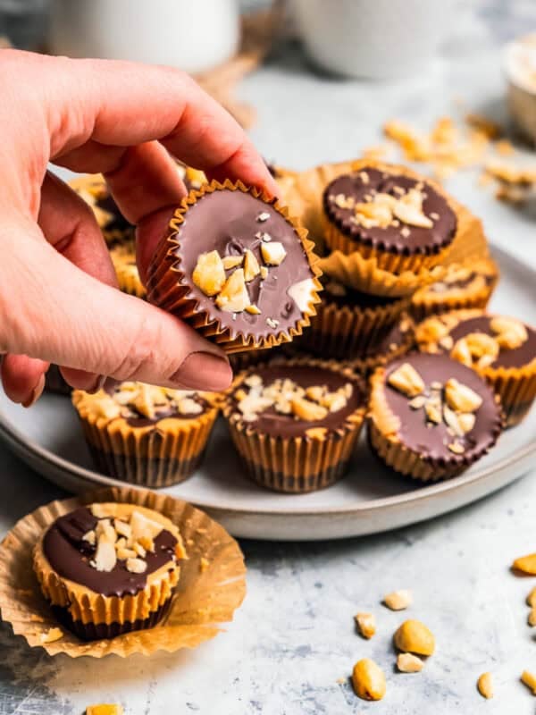 A hand lifting a peanut butter cup from a pile on a plate.