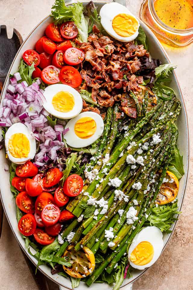 salad greens topped with chopped red onions, crumbled bacon, halved eggs, and asparagus spears