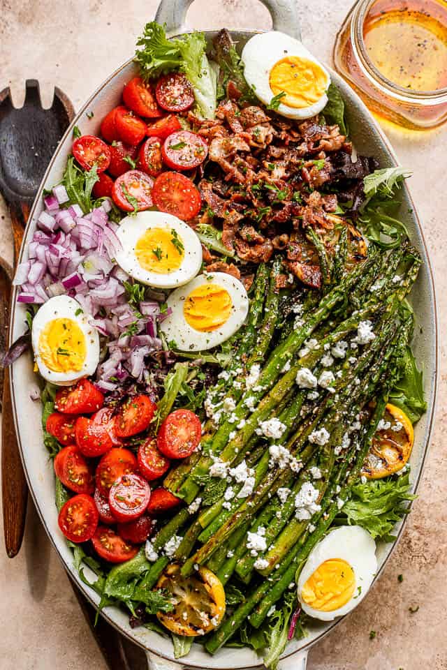 asparagus, eggs, bacon, and tomatoes on top of lettuce leaves in a long oval plate