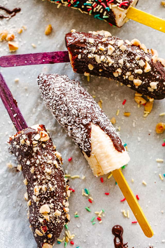 Bananas on a stick covered in chocolate and sprinkles of nuts and shredded coconut.