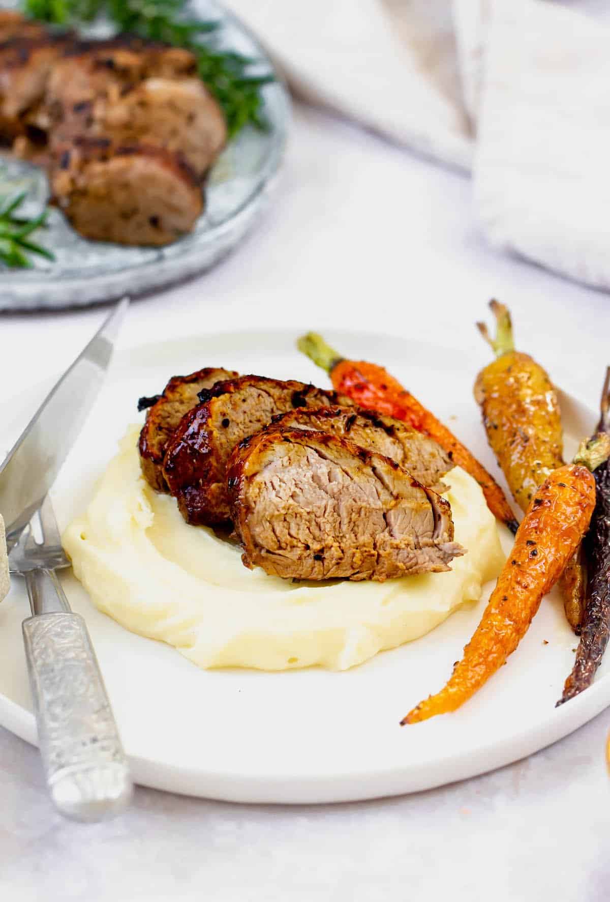 Slices of grilled pork on a bed of mashed potatoes with carrots.