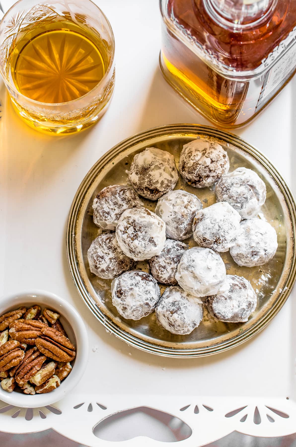 Bourbon Balls served on a platter, with a bottle of alcohol and a bowl of pecans arranged around the platter.