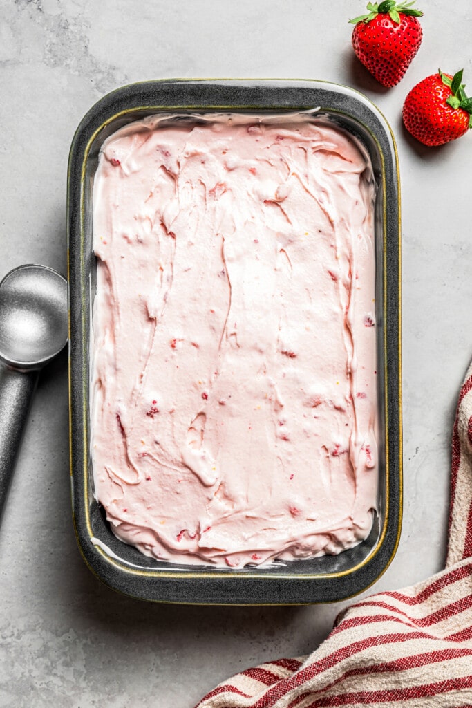 Overhead view of strawberry cheesecake ice cream in a loaf pan, next to an ice cream scoop.