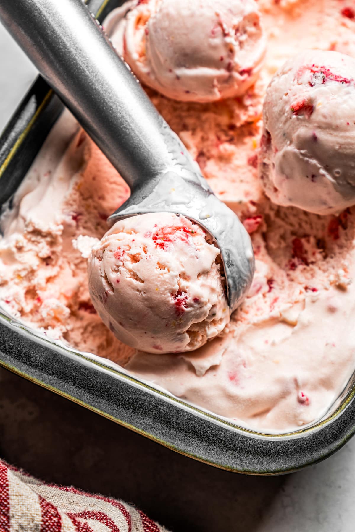 An ice cream scoop serving up a scoop of strawberry cheesecake ice cream from a loaf pan.