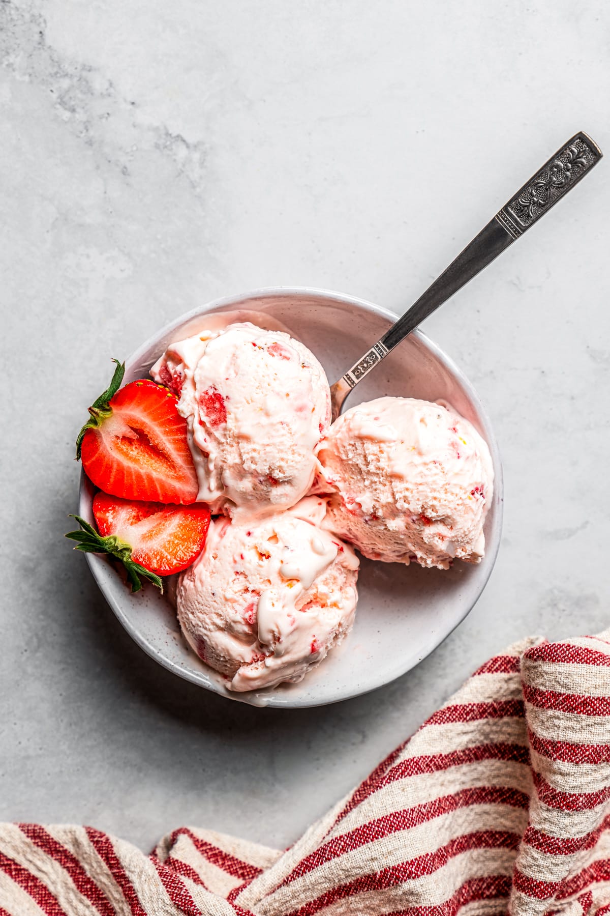 Overhead view of three scoops of strawberry cheesecake ice cream in a bowl garnished with fresh strawberries.