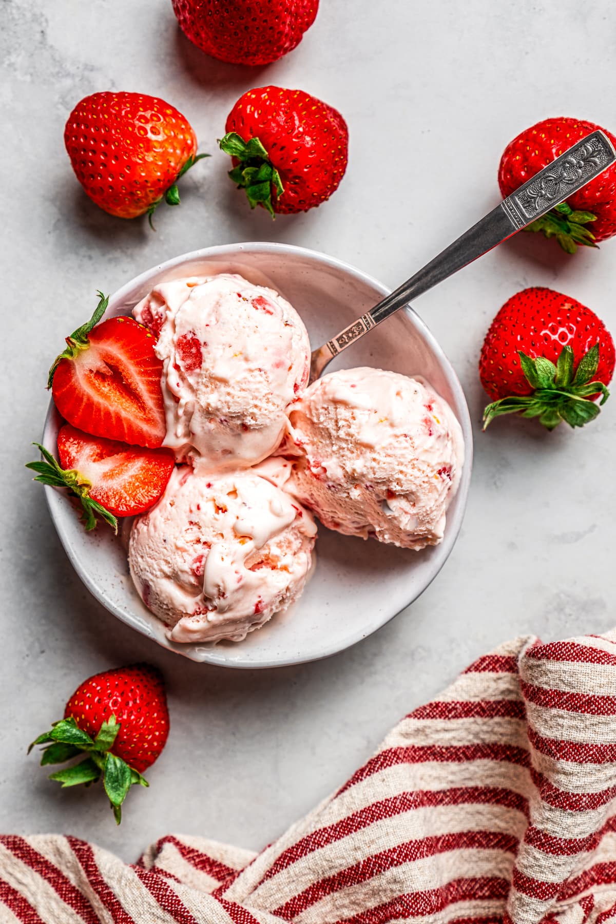 Overhead view of three scoops of strawberry cheesecake ice cream in a bowl garnished with fresh strawberries, surrounded by scattered berries.