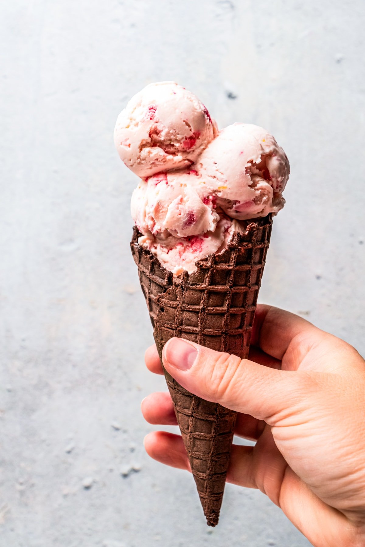 Hand holding up a waffle cone filled with three scoops of ice cream.