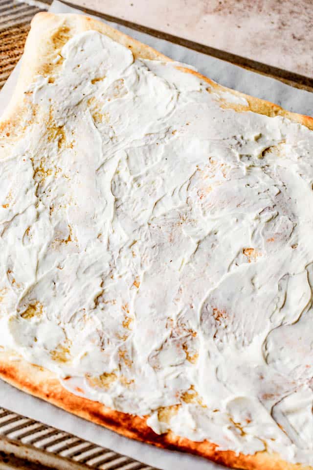 spreading cream cheese on top of grilled pizza dough