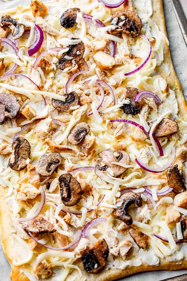 pizza dough topped with cheese, mushrooms, chicken and onions