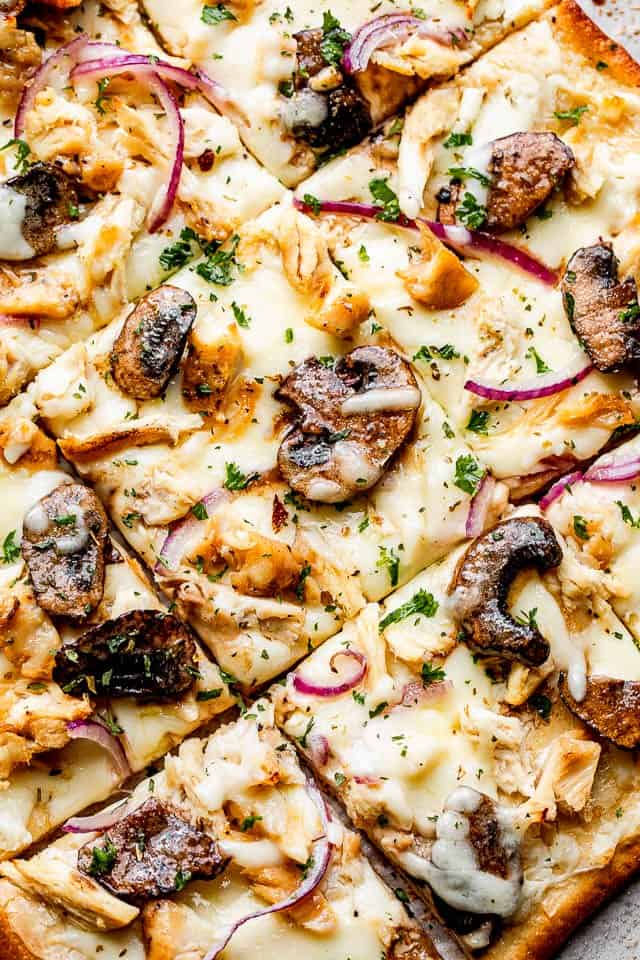 top view of a grilled pizza topped with Cheese, mushrooms, chicken, and red onions