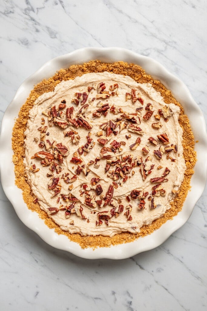 Toasted pecans added over top of Turtle pie filling spread into a Graham cracker pie crust in a pie plate.
