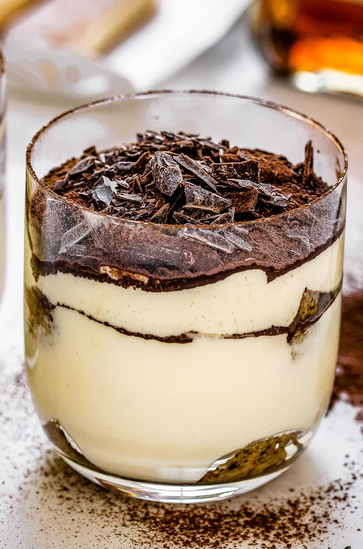 Cocoa powder is dusted over a glass of tiramisu.
