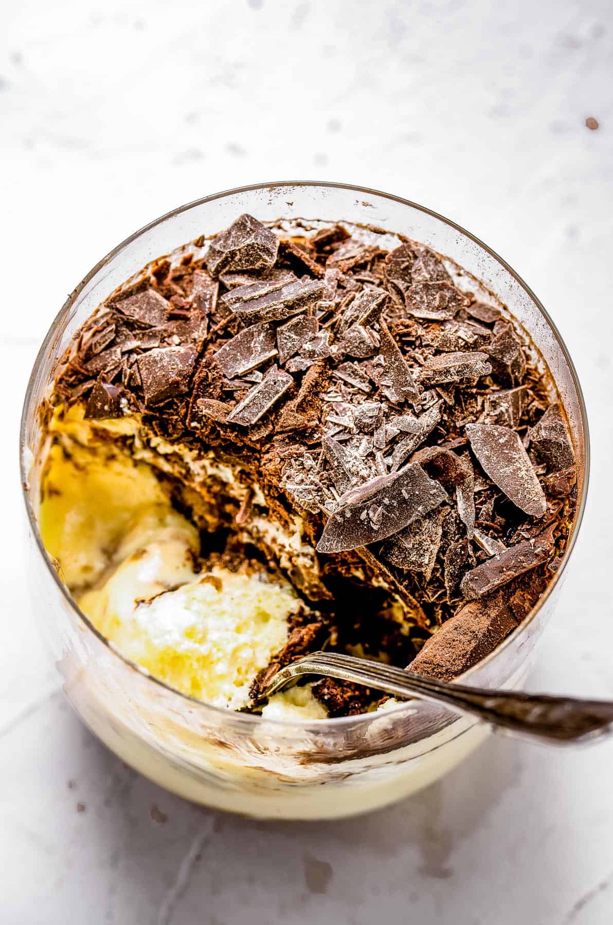 overhead shot of tiramisu in a glass with a spoon inside of it.