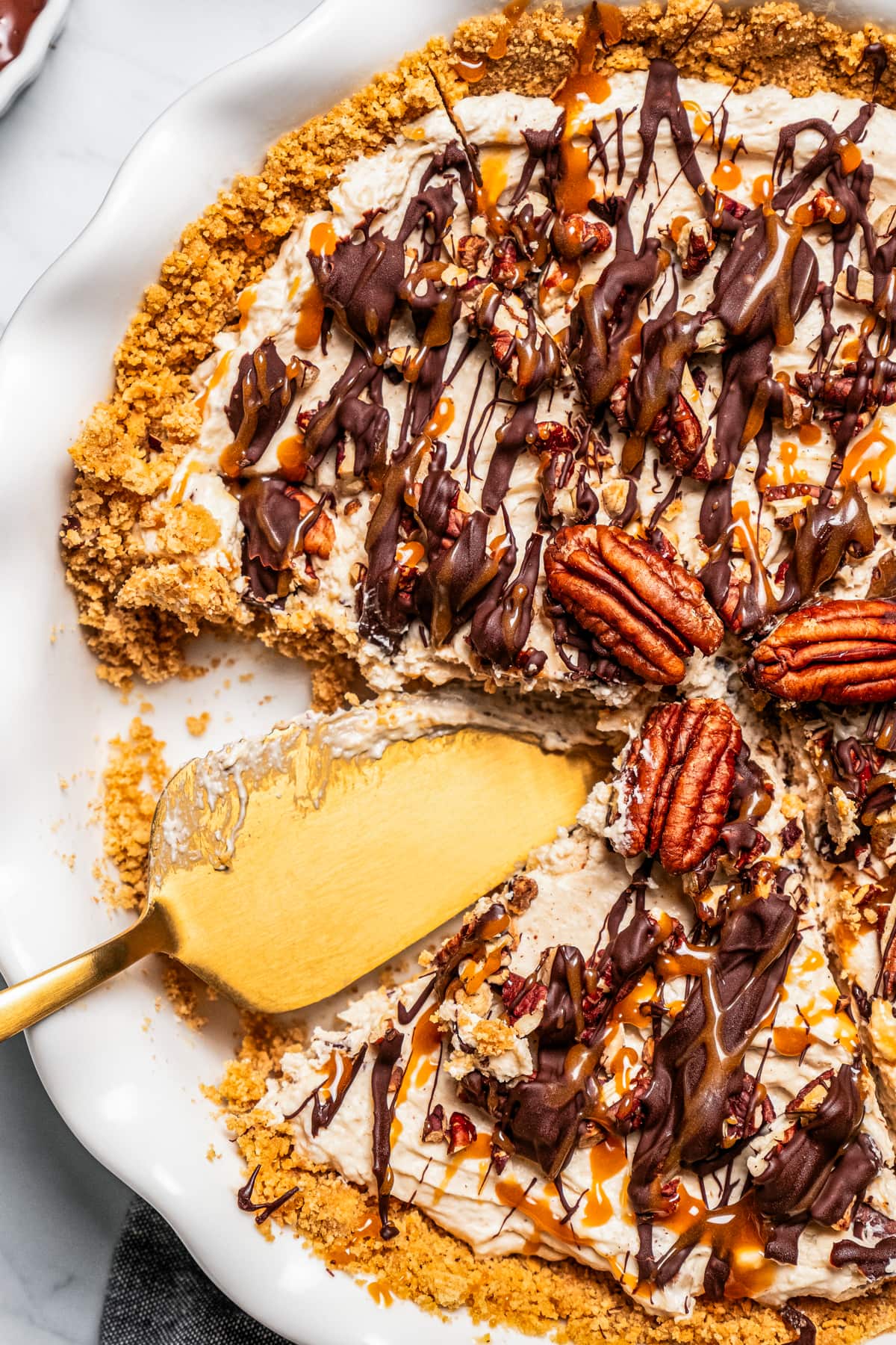 Overhead view of Turtle pie topped with toasted pecans and drizzled with caramel and chocolate, with a slice missing.