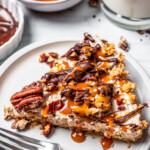A slice of Turtle pie on a white plate with a fork, next to bowls of toppings.