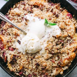 Overhead view of a homemade Brown Betty with peaches and cherries, topped with melted ice cream in a skillet.