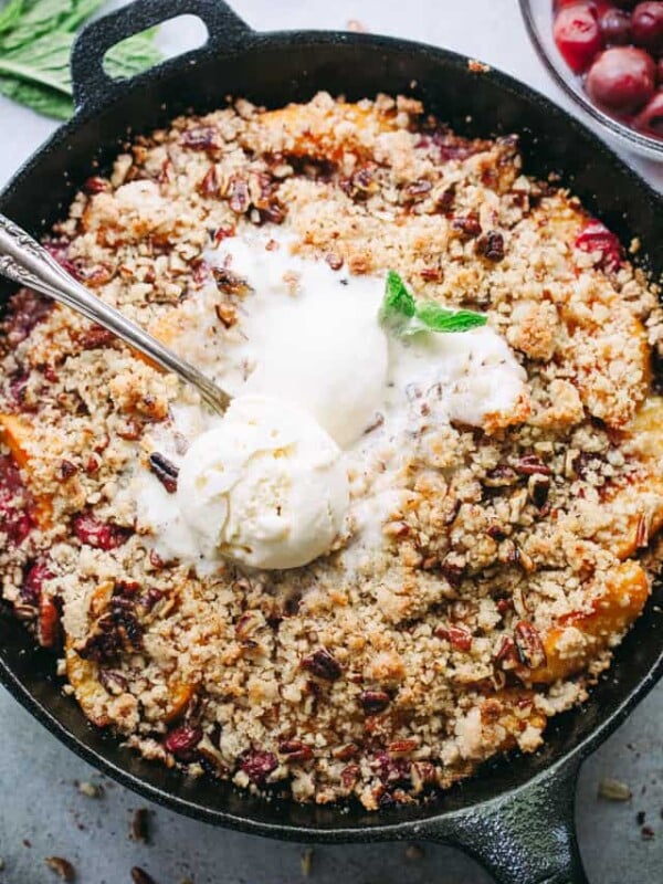 Overhead view of a homemade Brown Betty with peaches and cherries, topped with melted ice cream in a skillet.